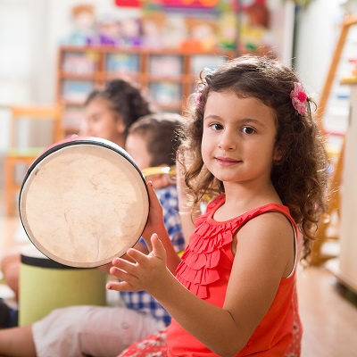 Little girl playing a drum looking at the camera