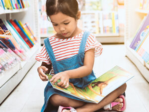 Little girl sat in a library on the floor reading a book