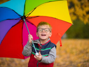 little boy smiling holding a rainbow coloured umbrella